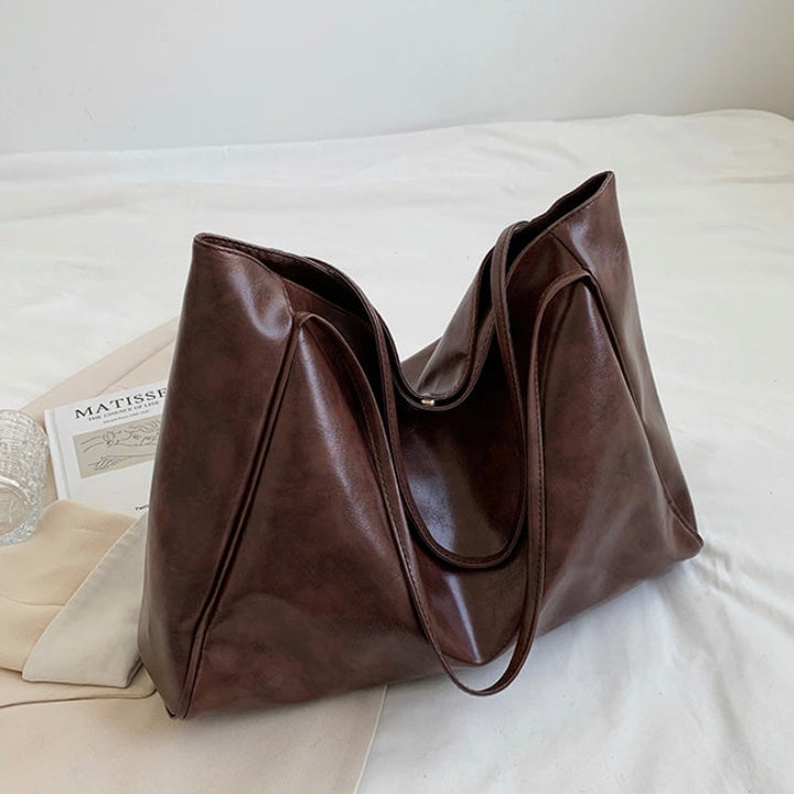 A woman wearing a glossy taupe shoulder bag over her shoulder at an evening occasion.