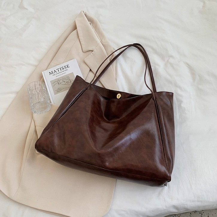 A woman wearing a glossy taupe shoulder bag over her shoulder at an evening occasion.