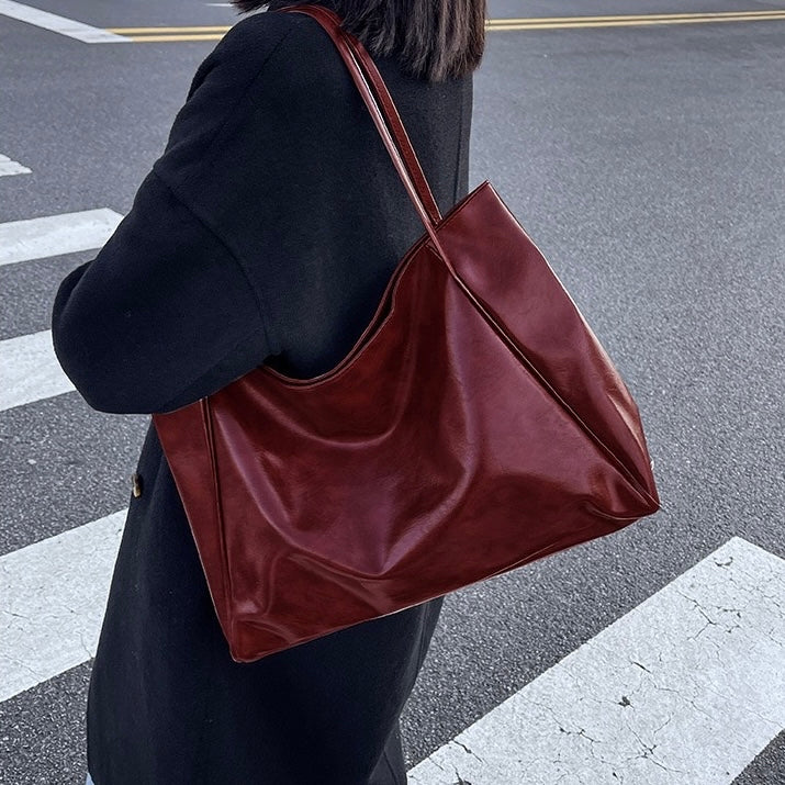 A woman wearing a glossy taupe shoulder bag over her shoulder at an evening occasion.