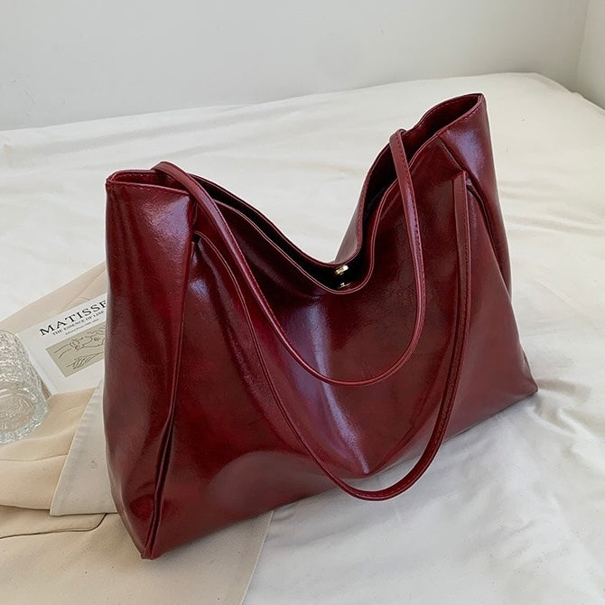 A woman wearing a glossy taupe shoulder bag over her shoulder at an evening occasion.