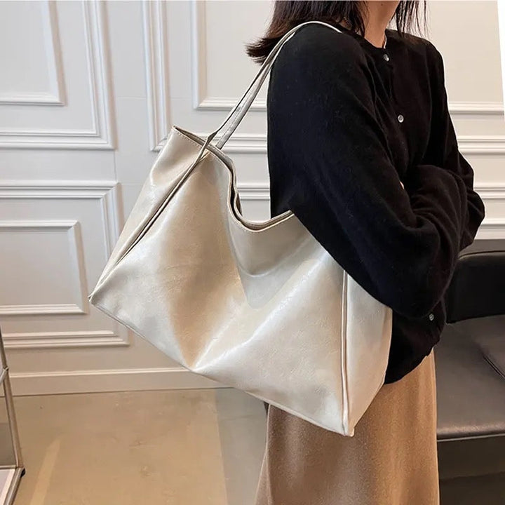 A woman wearing a glossy taupe shoulder bag over her shoulder at an evening occasion.