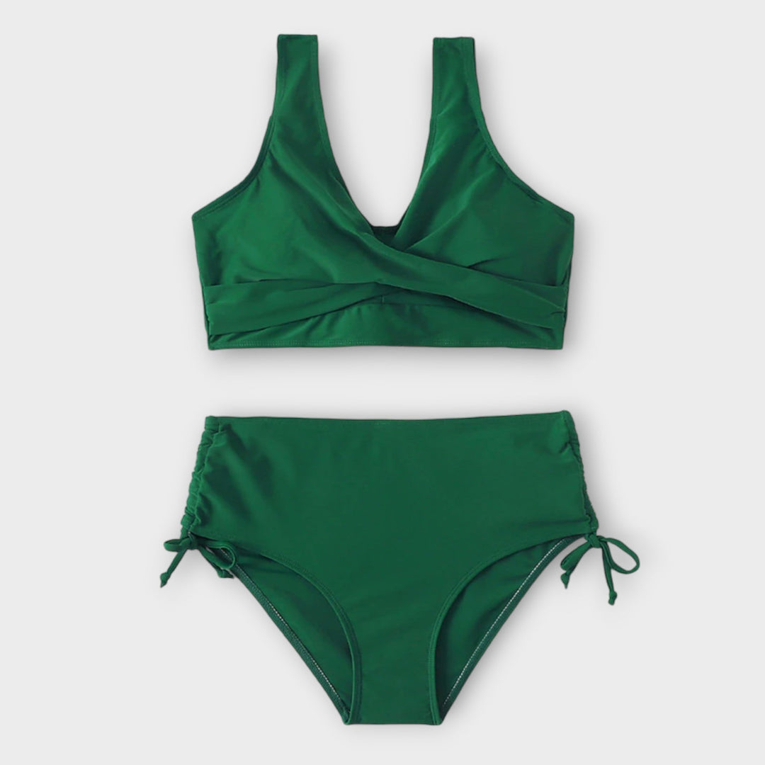 A woman in a plain green two-piece bikini set with a wrap front, relaxed and smiling in the sun.