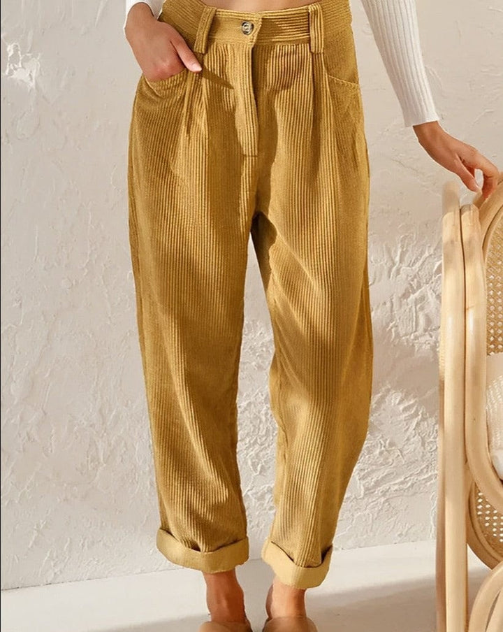 Woman wearing loose high-waisted pants with a tucked-in top, standing in soft light.