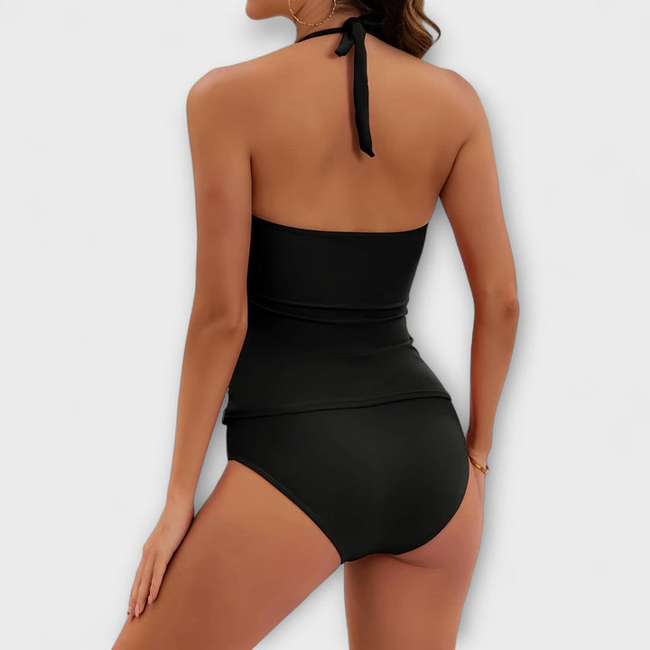 A woman by the water in a solid-colour two-piece halter swimsuit, relaxed and confident in the sun.