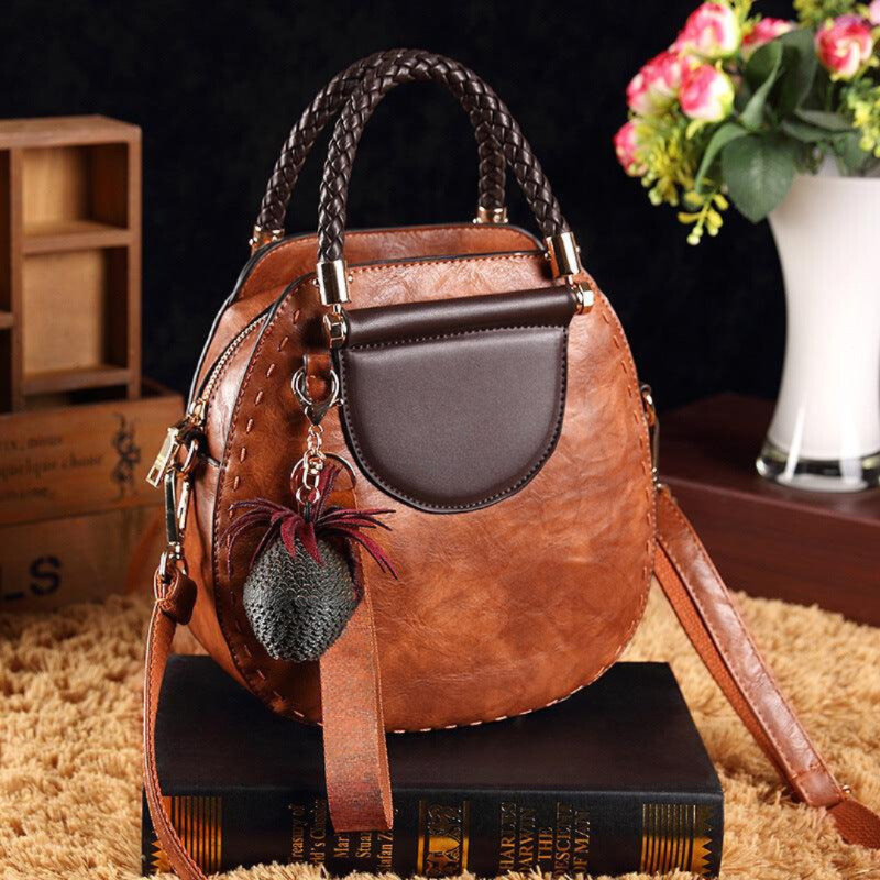 A woman carrying a small round top-handle handbag with a rich finish