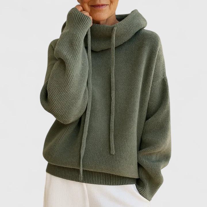 A woman wearing a cosy soft green hoodie with a drawstring hood and white pants.