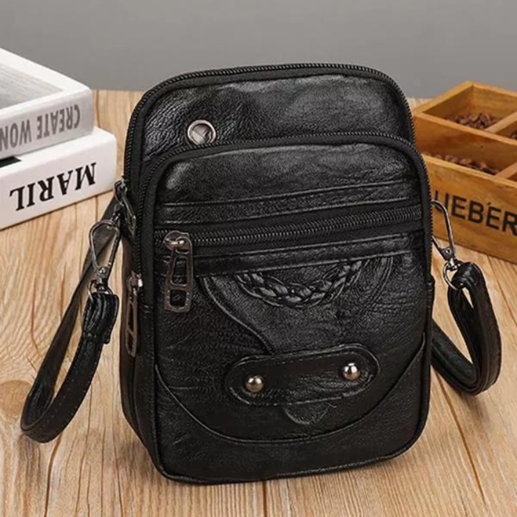 A small brown crossbody bag with a plaited front detail and zip pockets on a wooden stump.