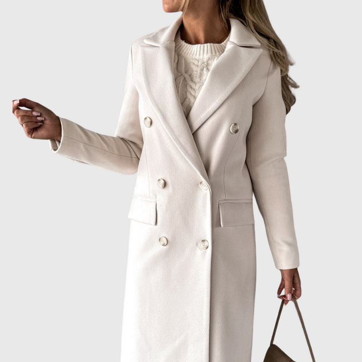 A woman wearing a long waisted coat, standing elegantly outdoors