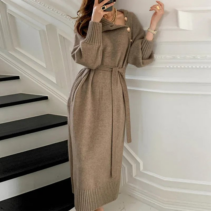 Woman in the Diana cosy wrap dress with gold-tone buttons and a waist tie, holding a warm drink at home.