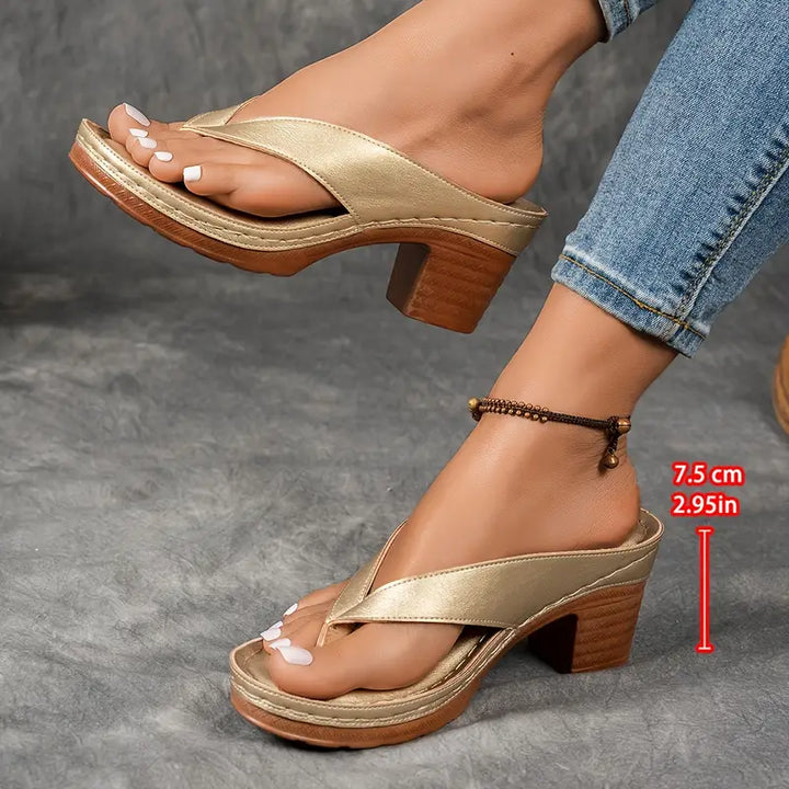 A woman wearing gold block heel sandals with a toe-post strap at an evening event.