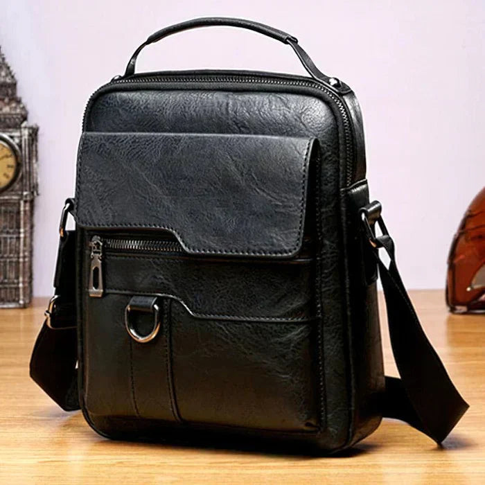 A tan crossbody bag with a flap front, zip pocket and wide adjustable strap on a wooden stump.