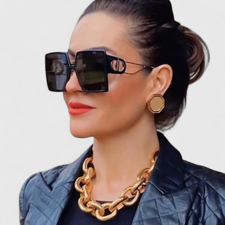 A woman wearing oversized D-frame sunglasses, looking confident and relaxed in the sunshine.