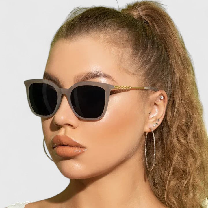 A woman on a coastal walk wearing oversized retro sunglasses, relaxed in the bright sun.