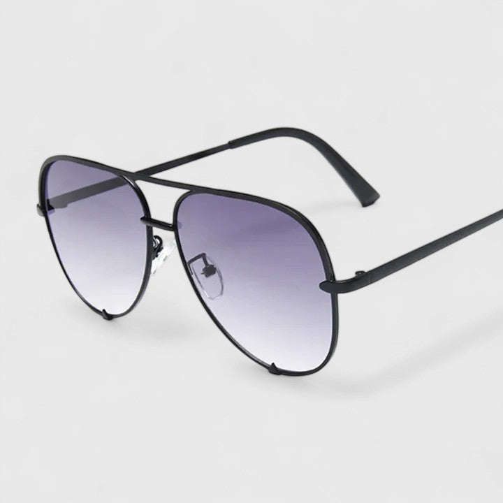 A woman by the sea wearing aviator sunglasses with gradient mirror lenses, relaxed in the sun.