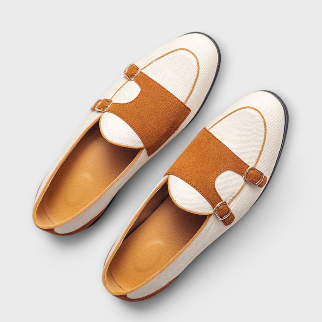 A woman wearing cream and tan round-toe slip-on loafers with twin gold buckle straps, walking with ease.