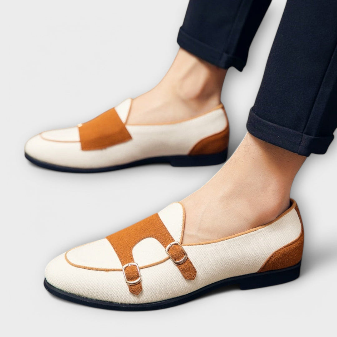 A woman wearing cream and tan round-toe slip-on loafers with twin gold buckle straps, walking with ease.