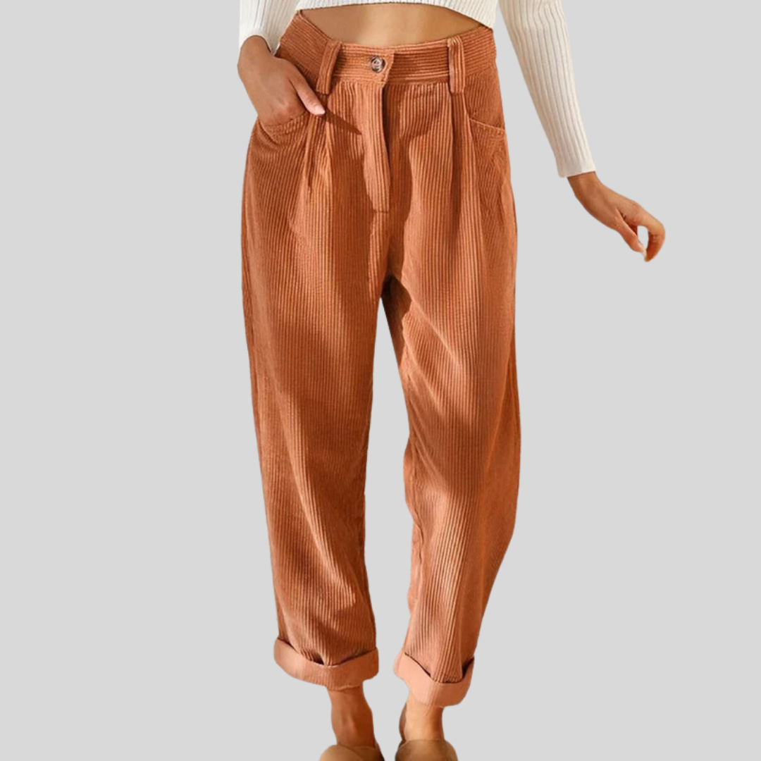 Woman wearing loose high-waisted pants with a tucked-in top, standing in soft light.