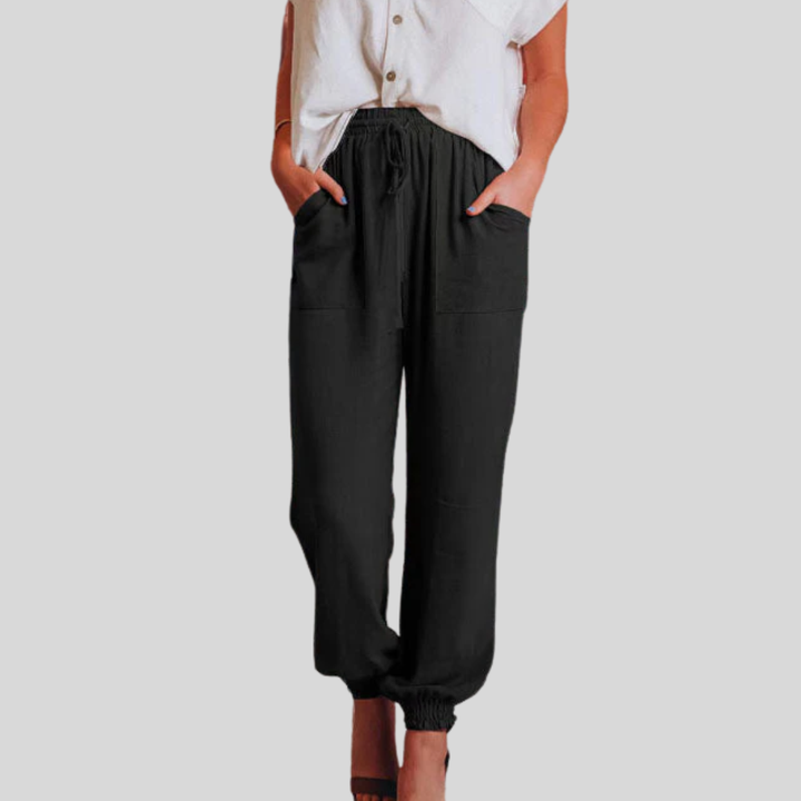 A woman wearing slim tapered black drawstring joggers with a high waist and front patch pockets.