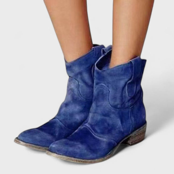 Woman wearing brown Western ankle boots with jeans, standing on a country lane.