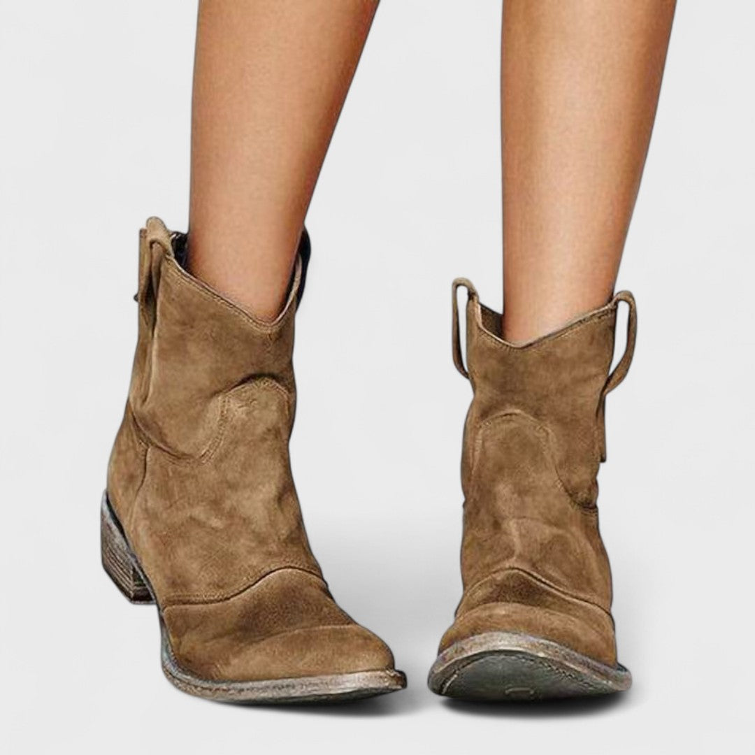 Woman wearing brown Western ankle boots with jeans, standing on a country lane.