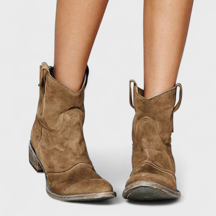 Woman wearing brown Western ankle boots with jeans, standing on a country lane.