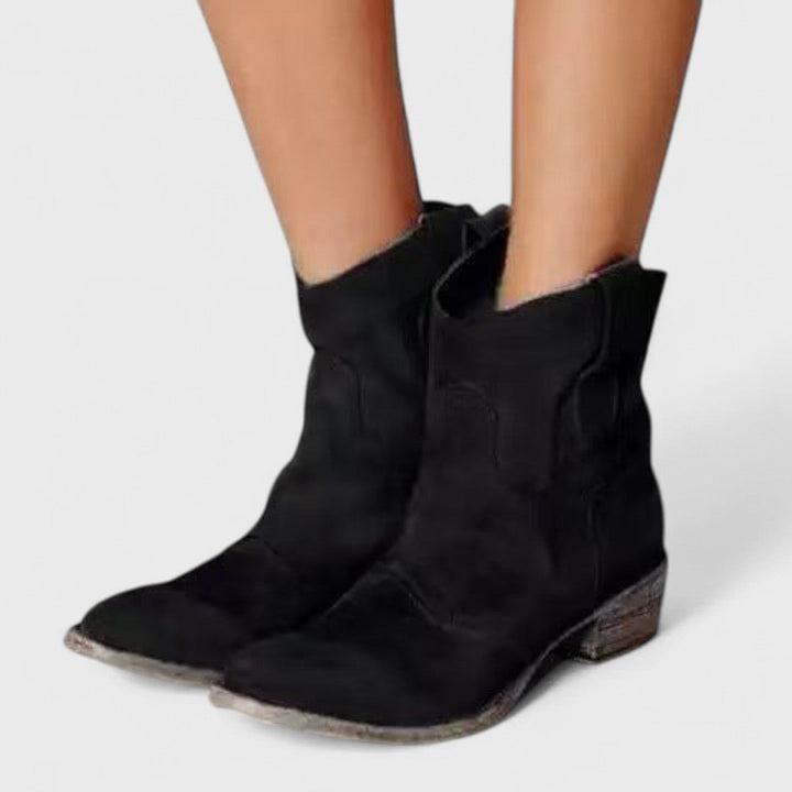 Woman wearing brown Western ankle boots with jeans, standing on a country lane.