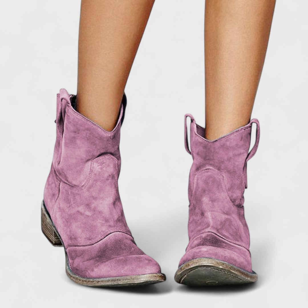 Woman wearing brown Western ankle boots with jeans, standing on a country lane.