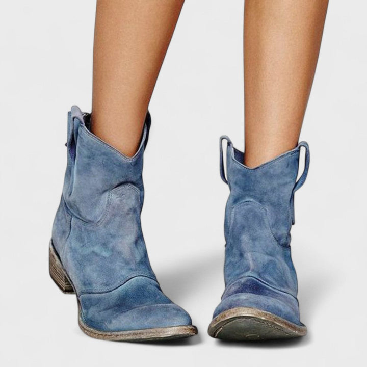 Woman wearing brown Western ankle boots with jeans, standing on a country lane.