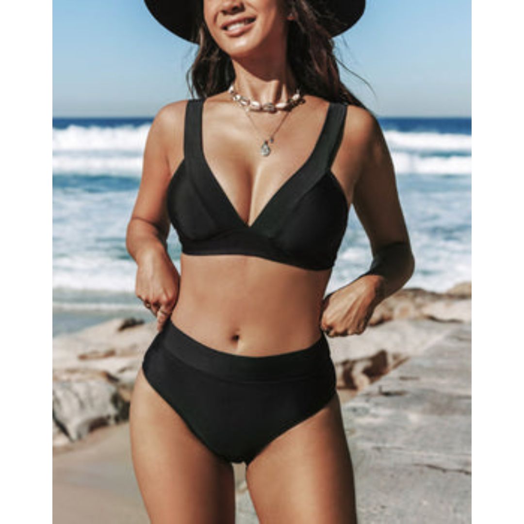 A woman standing in the sun in a plain black bikini set with high-waist bottoms, relaxed and confident.