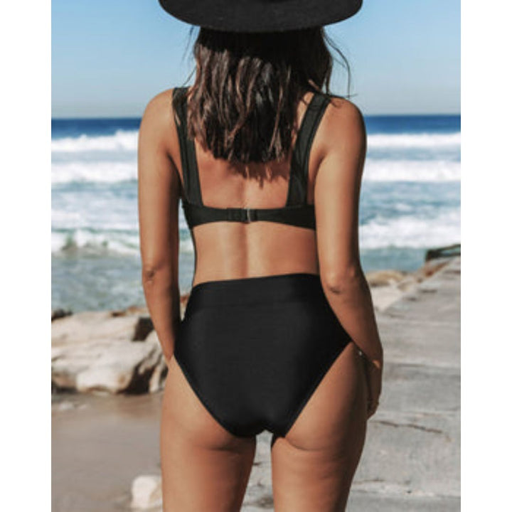 A woman standing in the sun in a plain black bikini set with high-waist bottoms, relaxed and confident.