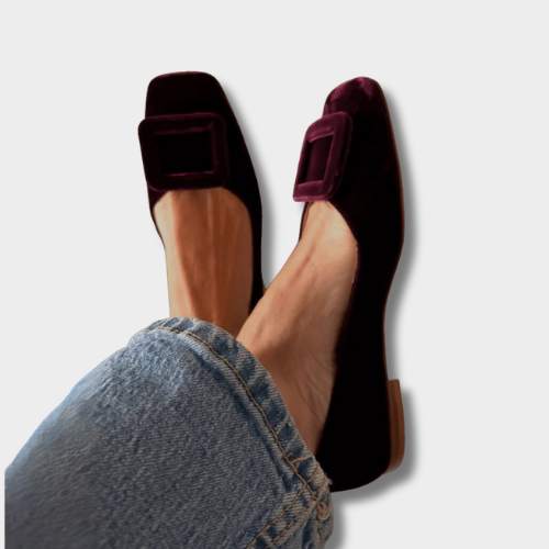 A woman wearing soft, velvety-finish loafers in a rich tone with tailored pants, looking refined and relaxed.