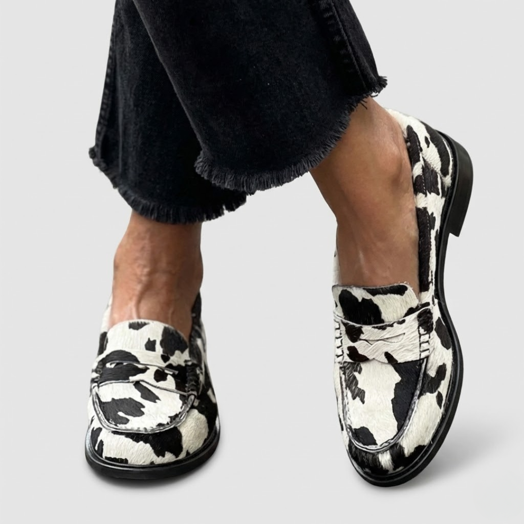 A woman wearing striking black-and-white cow-print loafers with dark jeans, standing confidently.