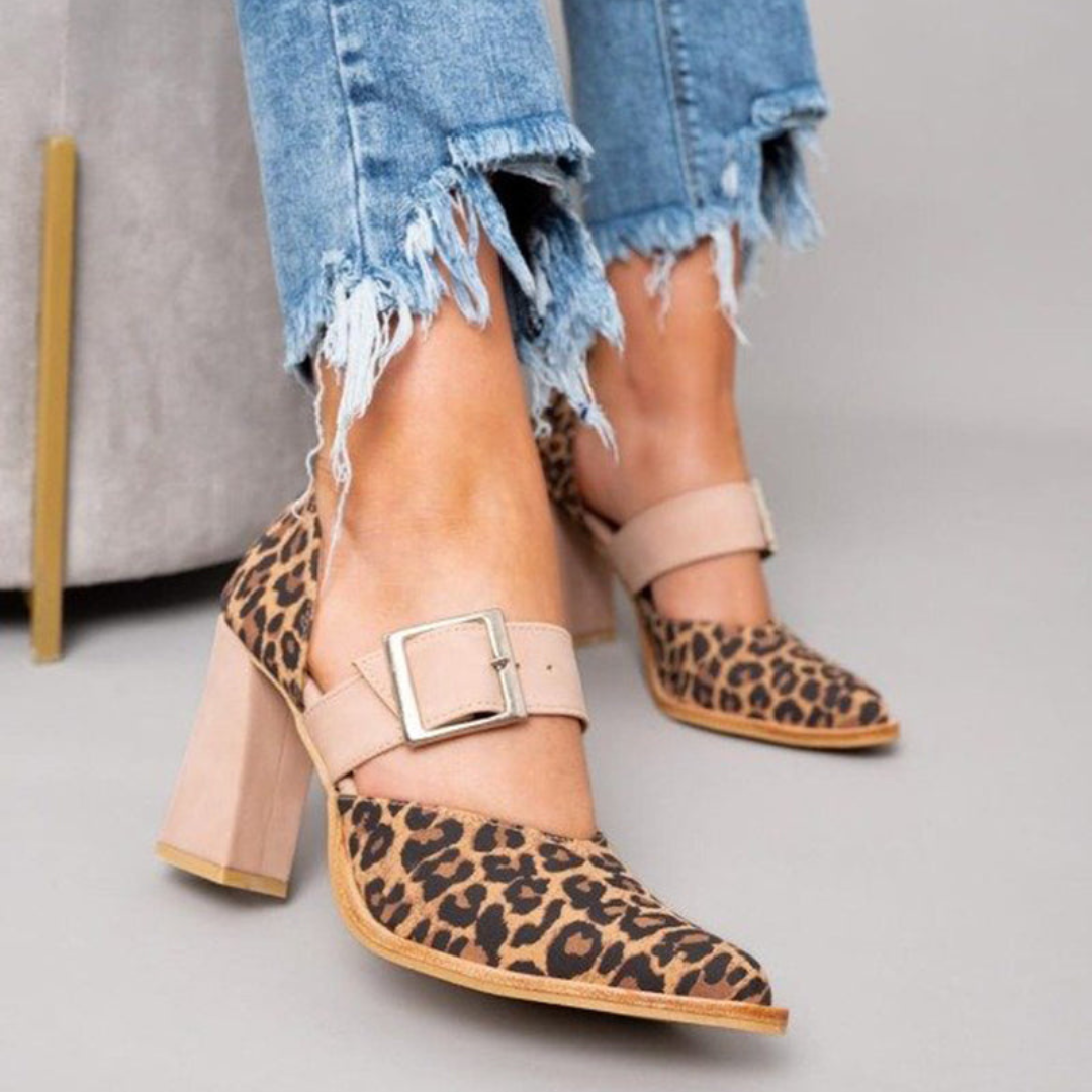 A woman wearing leopard-print pointed heels with a neutral buckled strap and block heel, stepping out in a polished outfit.
