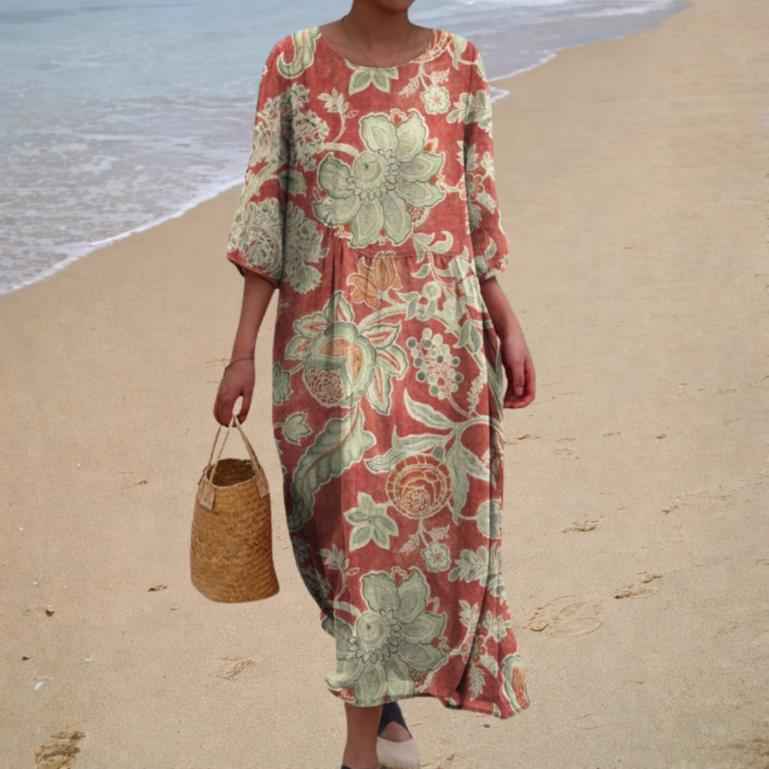 A woman wearing a long, flowing patterned dress that moves gently as she walks outdoors.