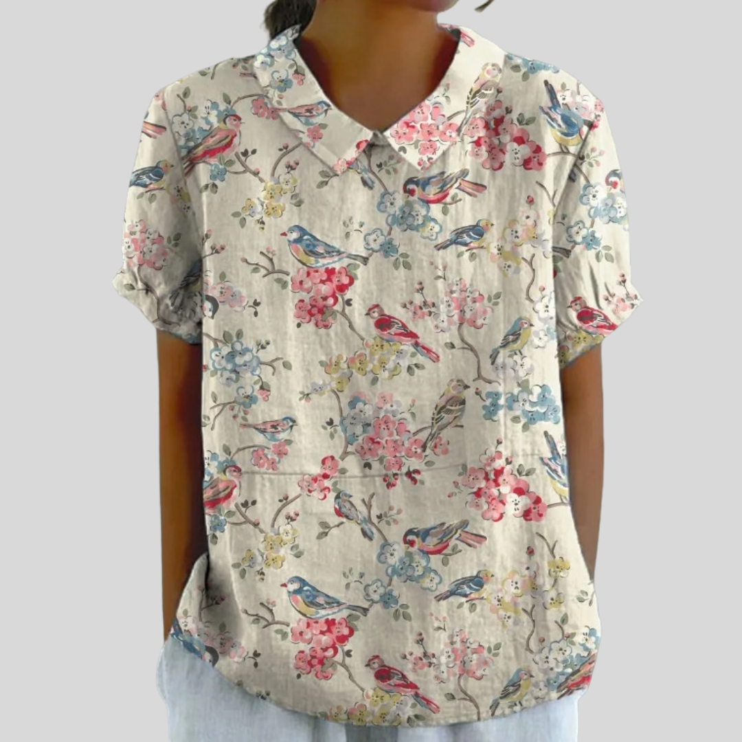 A woman wearing a soft cream polo collar top with a bird-and-blossom print, looking effortlessly feminine.