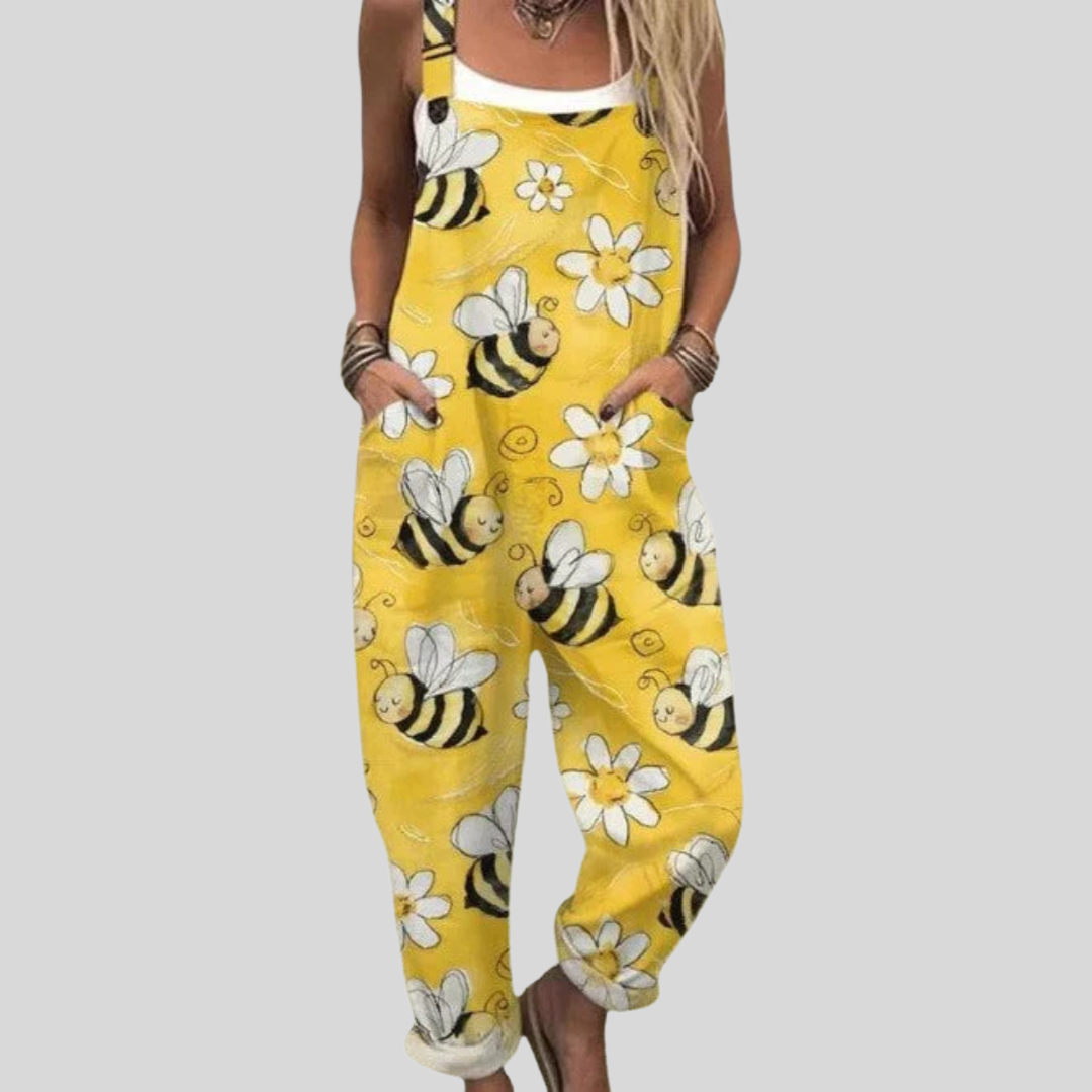 A woman wearing bright yellow overalls printed with bees and white daisies, smiling on a sunny day.