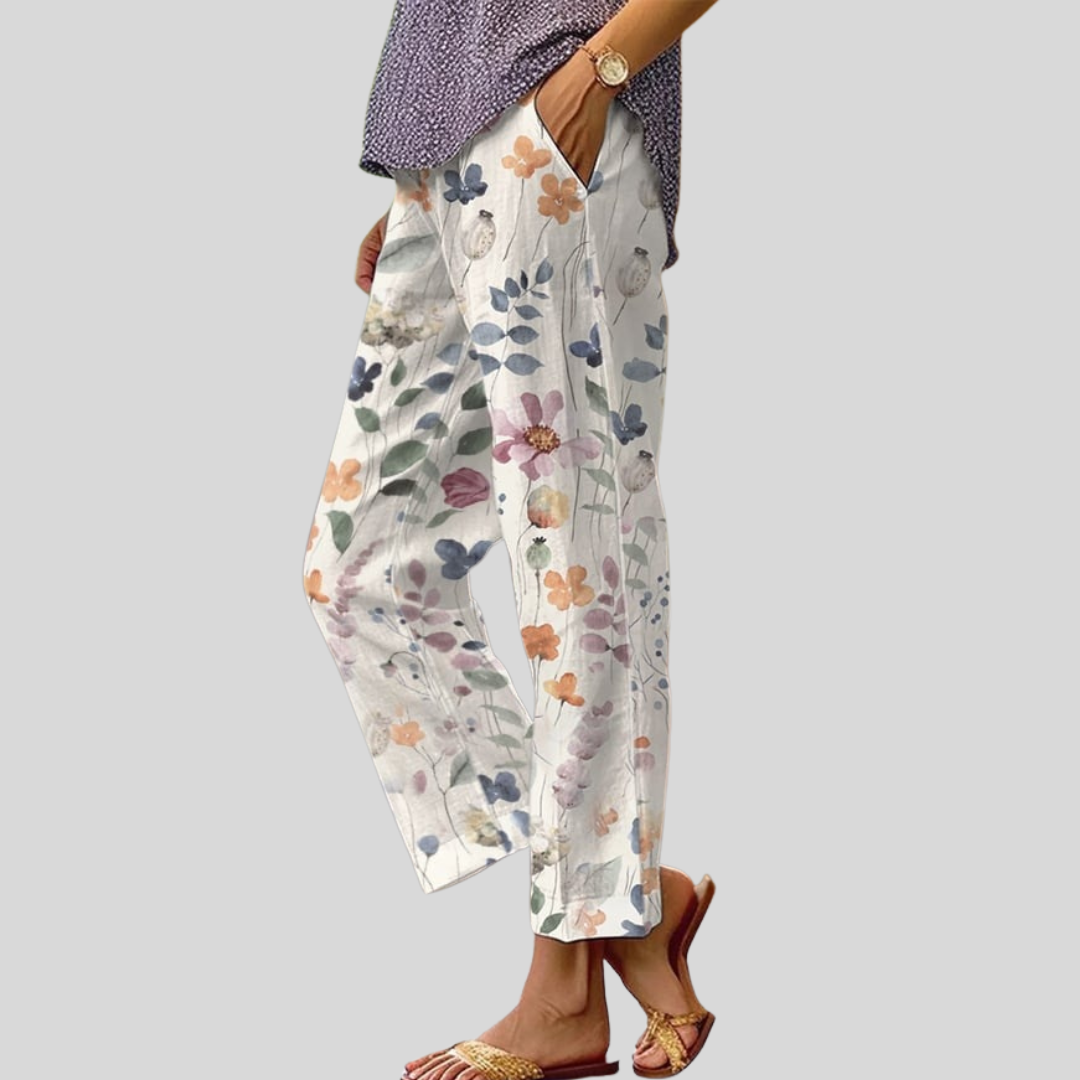 A woman wearing white pants with a soft watercolour floral print, elastic waist and deep pockets.