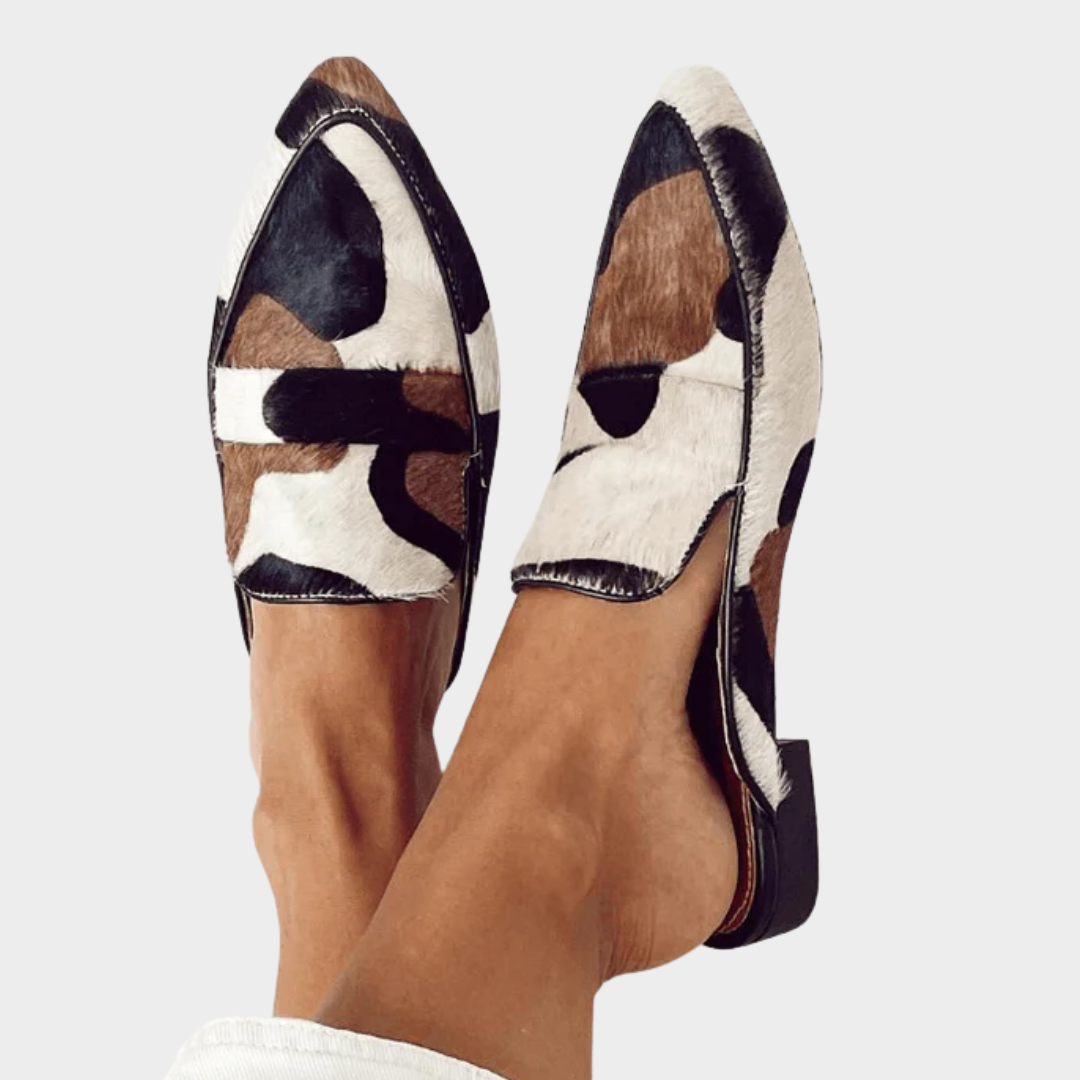 A woman wearing pointed cow-print loafers in warm brown, black and cream