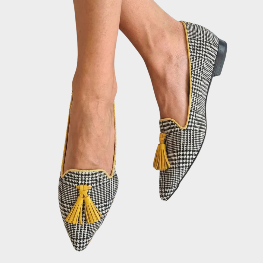 A woman wearing black-and-white check loafers with bright yellow tassels, looking cheerful and pulled together.
