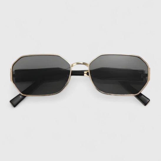 A woman wearing bold geometric gold-accented sunglasses with gradient lenses on a bright day.