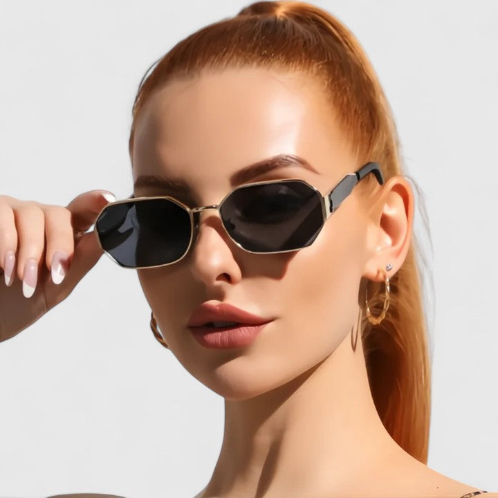 A woman wearing bold geometric gold-accented sunglasses with gradient lenses on a bright day.