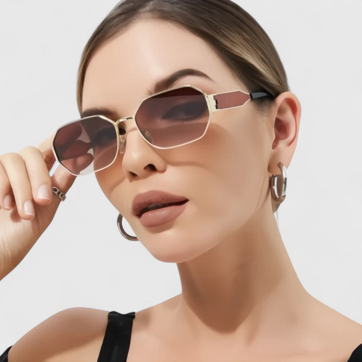 A woman wearing bold geometric gold-accented sunglasses with gradient lenses on a bright day.