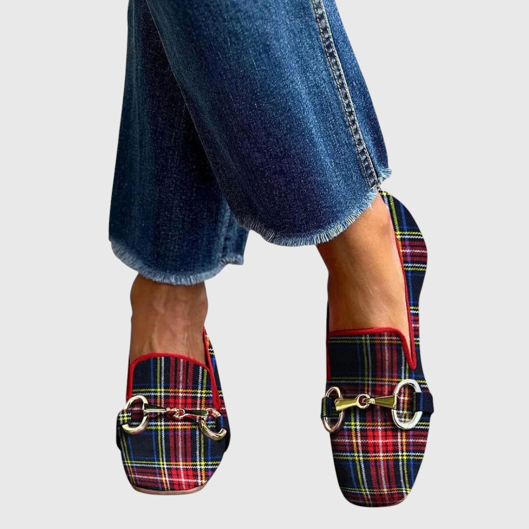 A woman wearing tartan check loafers with a gold horsebit detail and a smart outfit