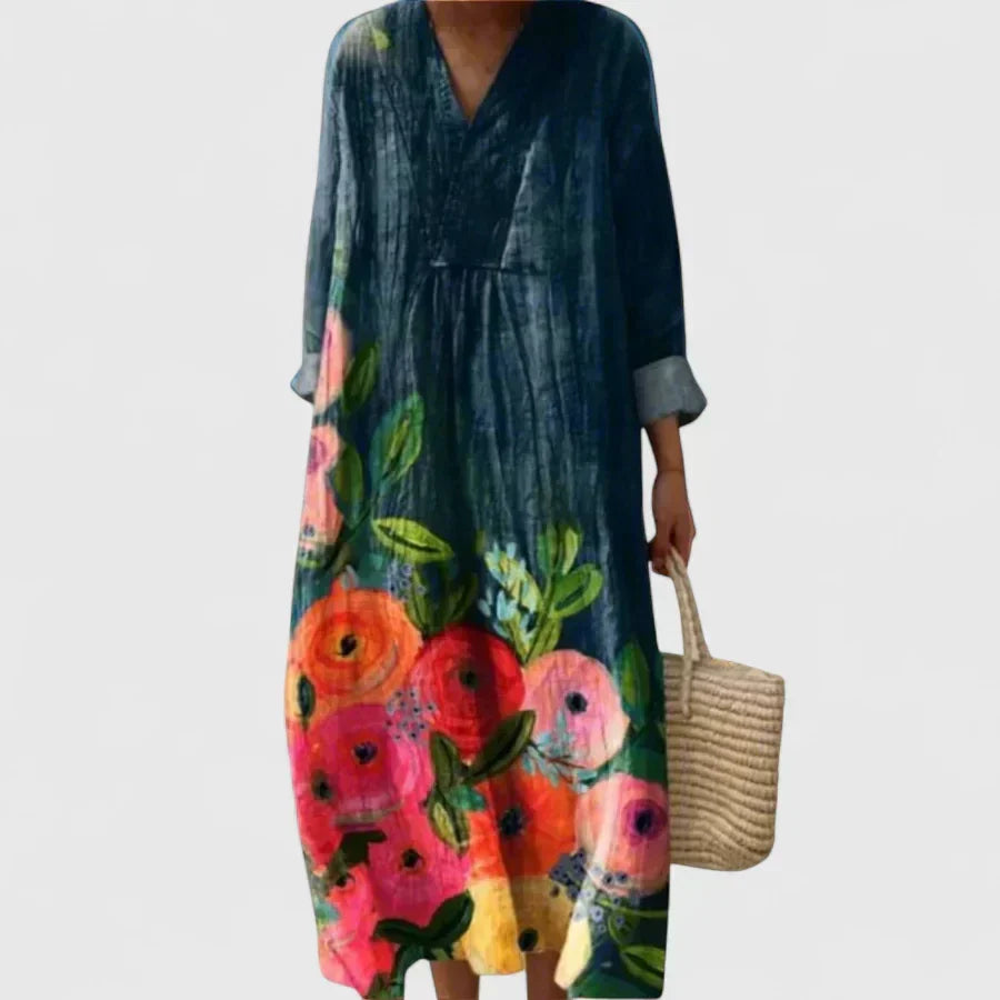 Woman wearing a long deep-blue maxi dress with bold pink and coral blooms and relaxed sleeves.