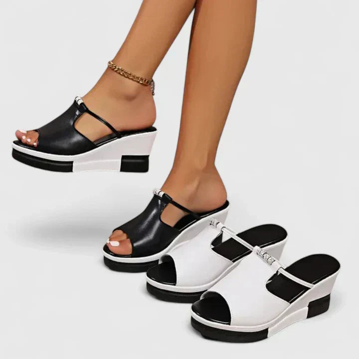 Black and white platform wedge mules with an open toe and a cut-out band across the front.
