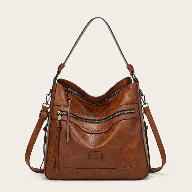 A soft brown vintage shoulder bag with zip pockets and tassel pulls, carried on the shoulder in town.