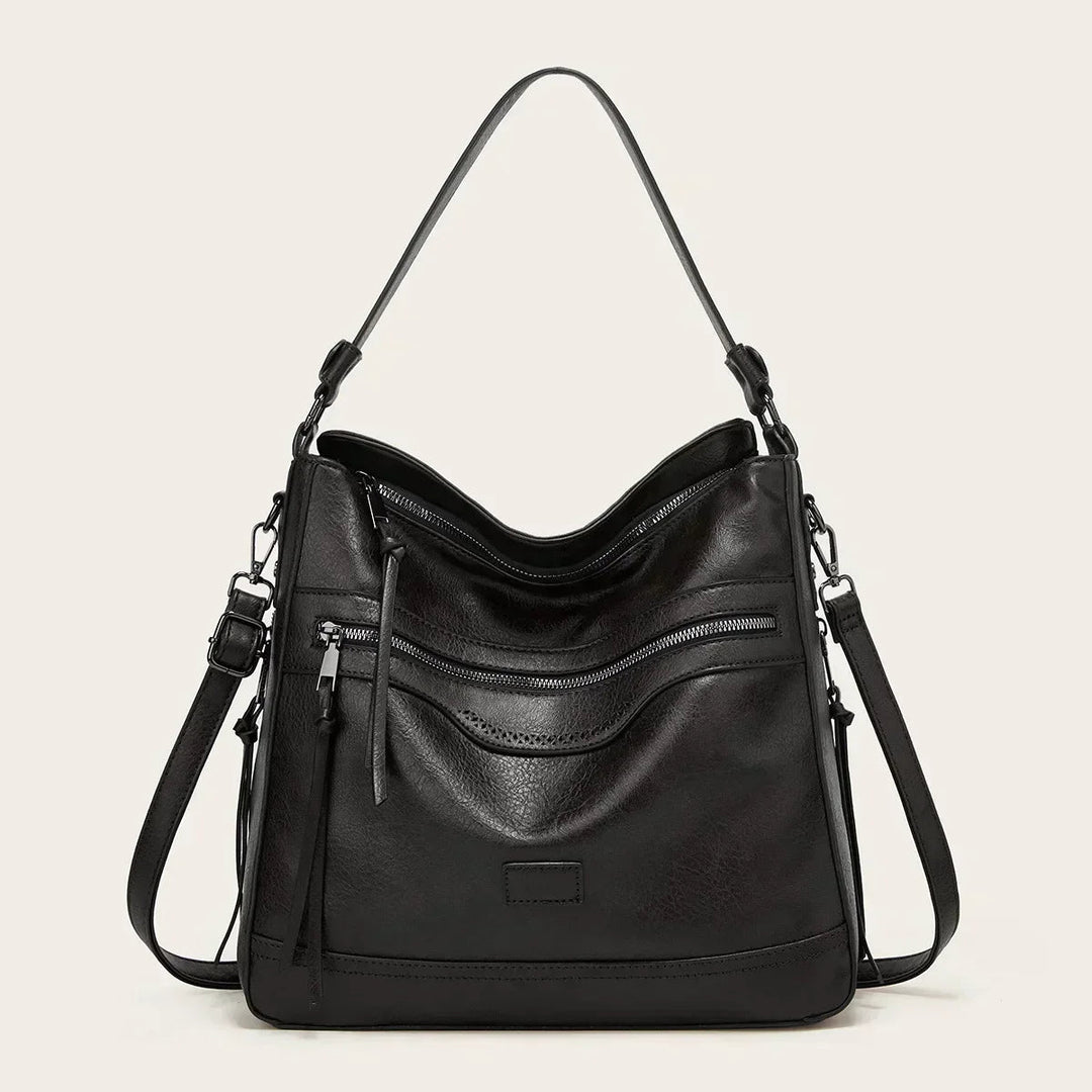 A soft brown vintage shoulder bag with zip pockets and tassel pulls, carried on the shoulder in town.
