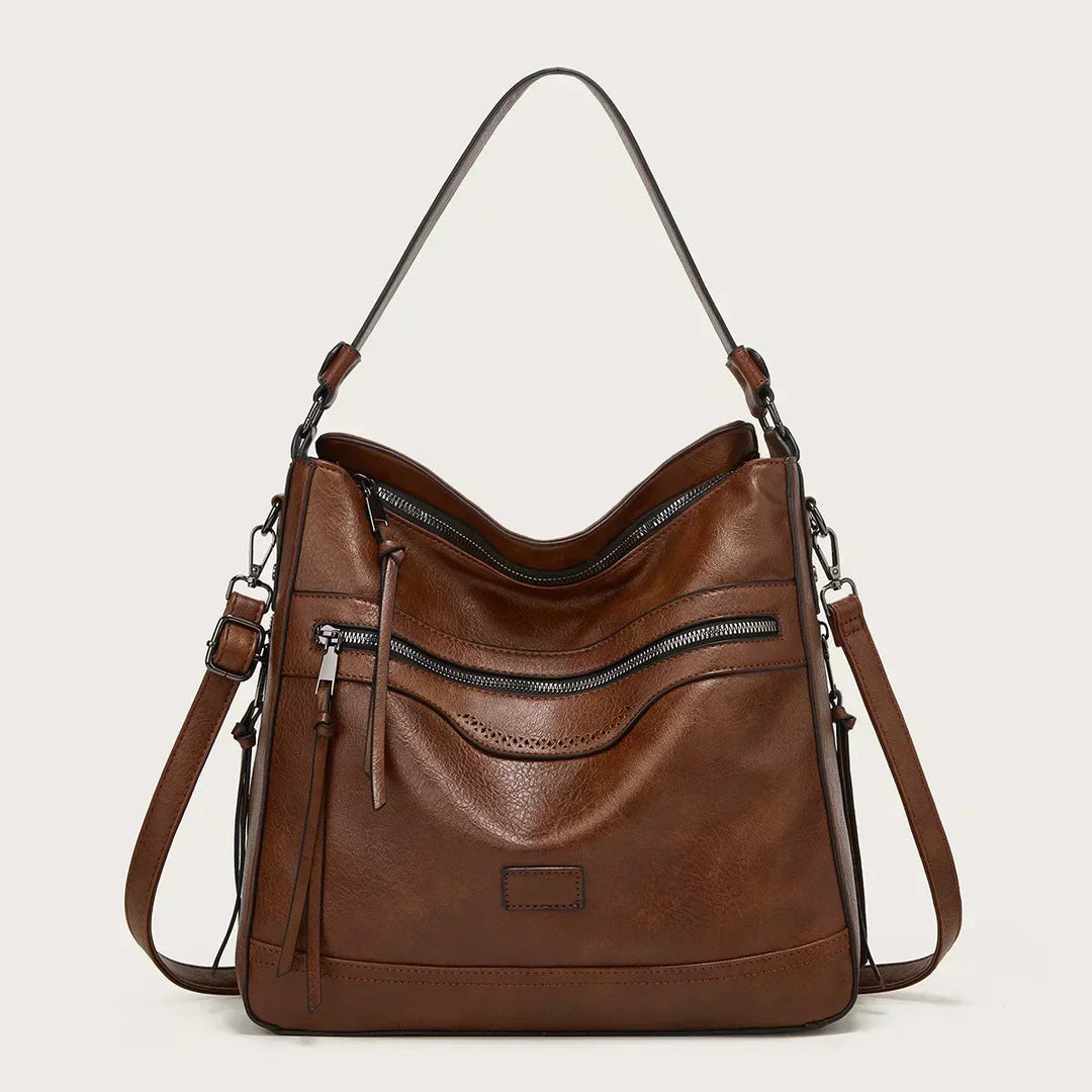 A soft brown vintage shoulder bag with zip pockets and tassel pulls, carried on the shoulder in town.
