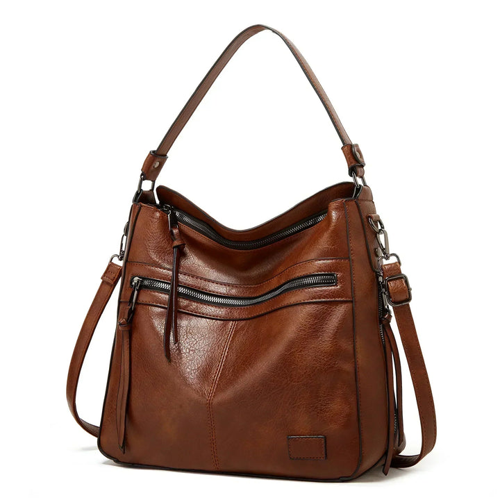 A soft brown vintage shoulder bag with zip pockets and tassel pulls, carried on the shoulder in town.