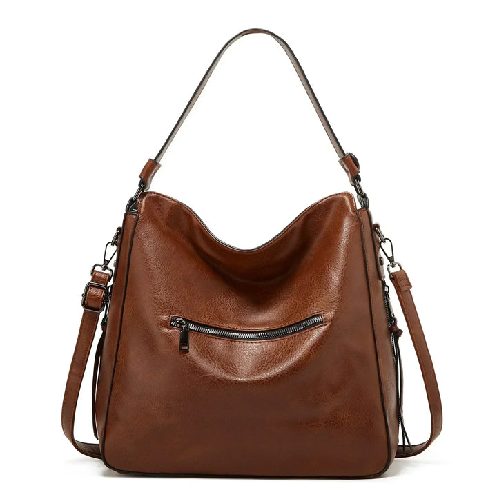 A soft brown vintage shoulder bag with zip pockets and tassel pulls, carried on the shoulder in town.